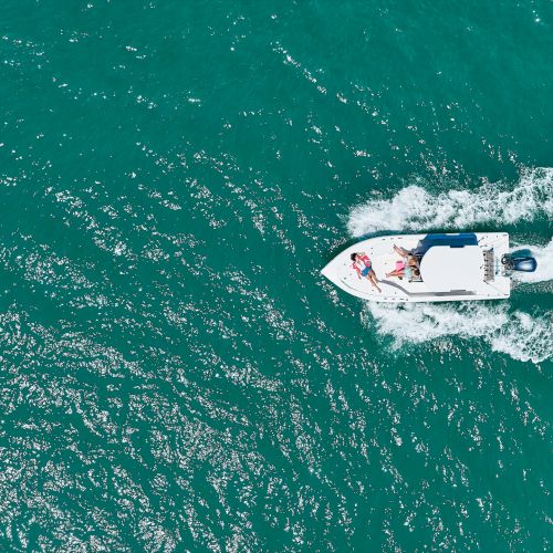 An aerial view of a speedboat racing across turquoise water, leaving a foamy wake behind it as people enjoy the ride.