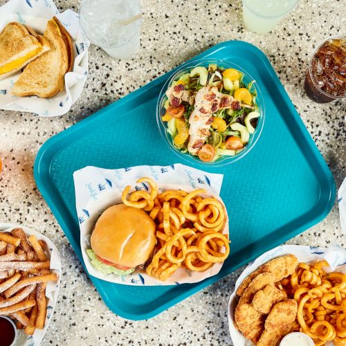 A blue meal tray with salad, burger and fries, plus drinks and sides like garlic bread and cookies.