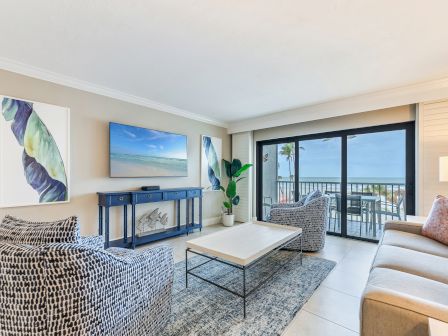 Bright living room with beach-themed art and a blue console, plus sliding doors revealing an ocean balcony view.