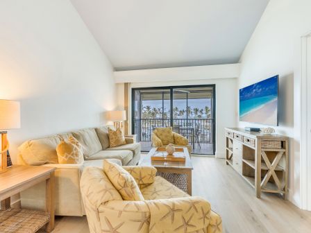 Bright coastal living room with a sofa, coffee table, TV, and a framed ocean scene by sliding doors.
