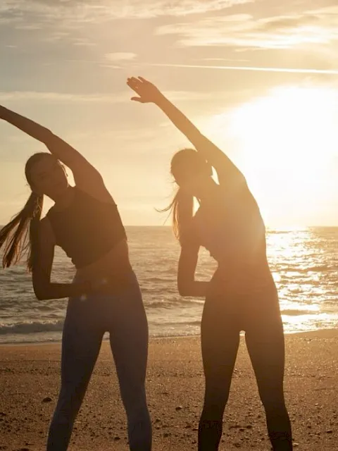 Two women stretching on the beach at sunset.