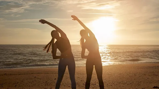 Two women stretching on the beach at sunset.