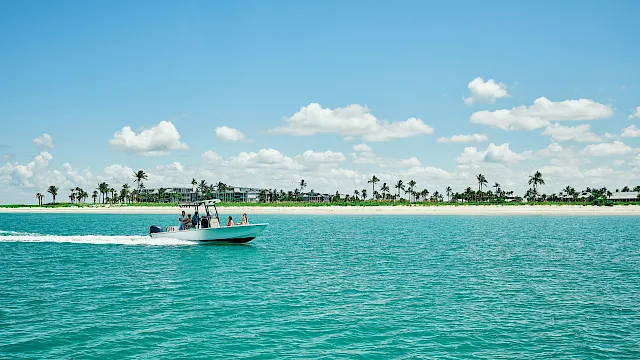 A boat cruising across turquoise water in front of the South Seas beach and palm-lined resort.